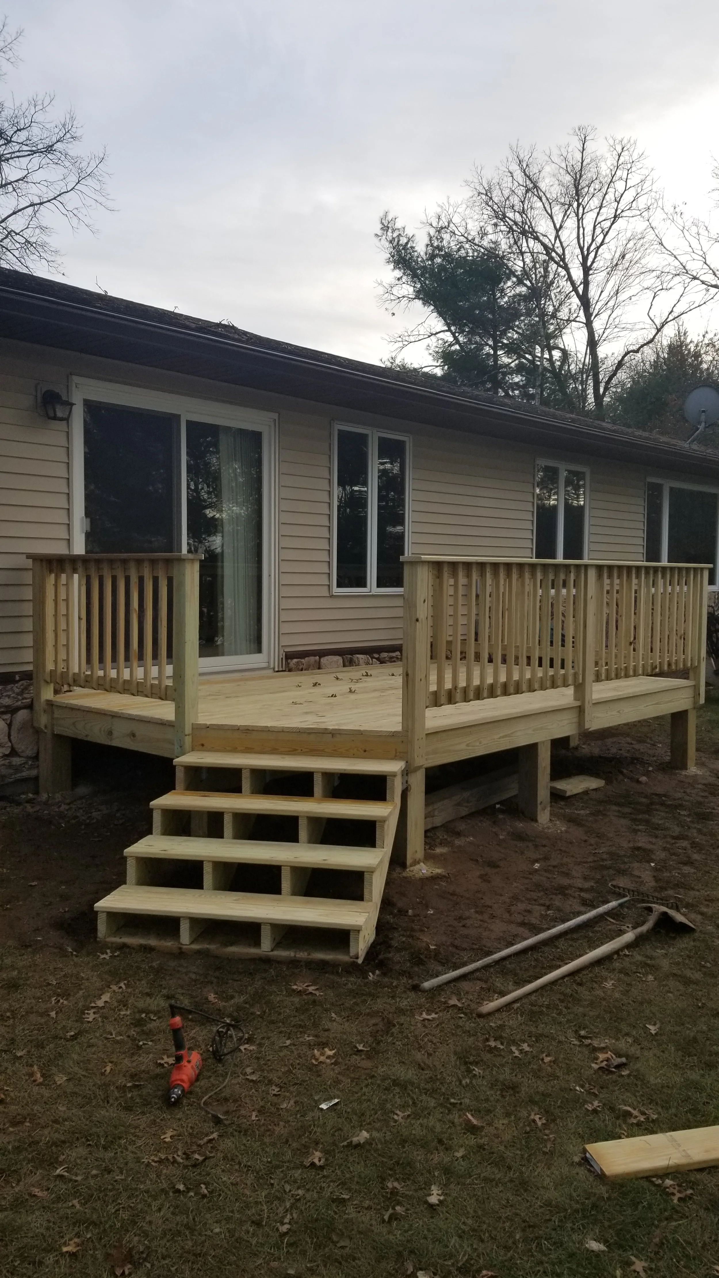 Wooden deck under construction attached to a house with sliding door and window, with tools on the ground.