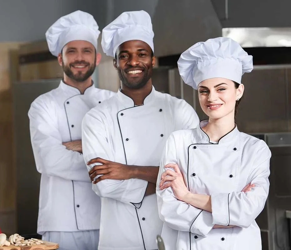 Three chefs in white uniforms and hats, standing in a kitchen.