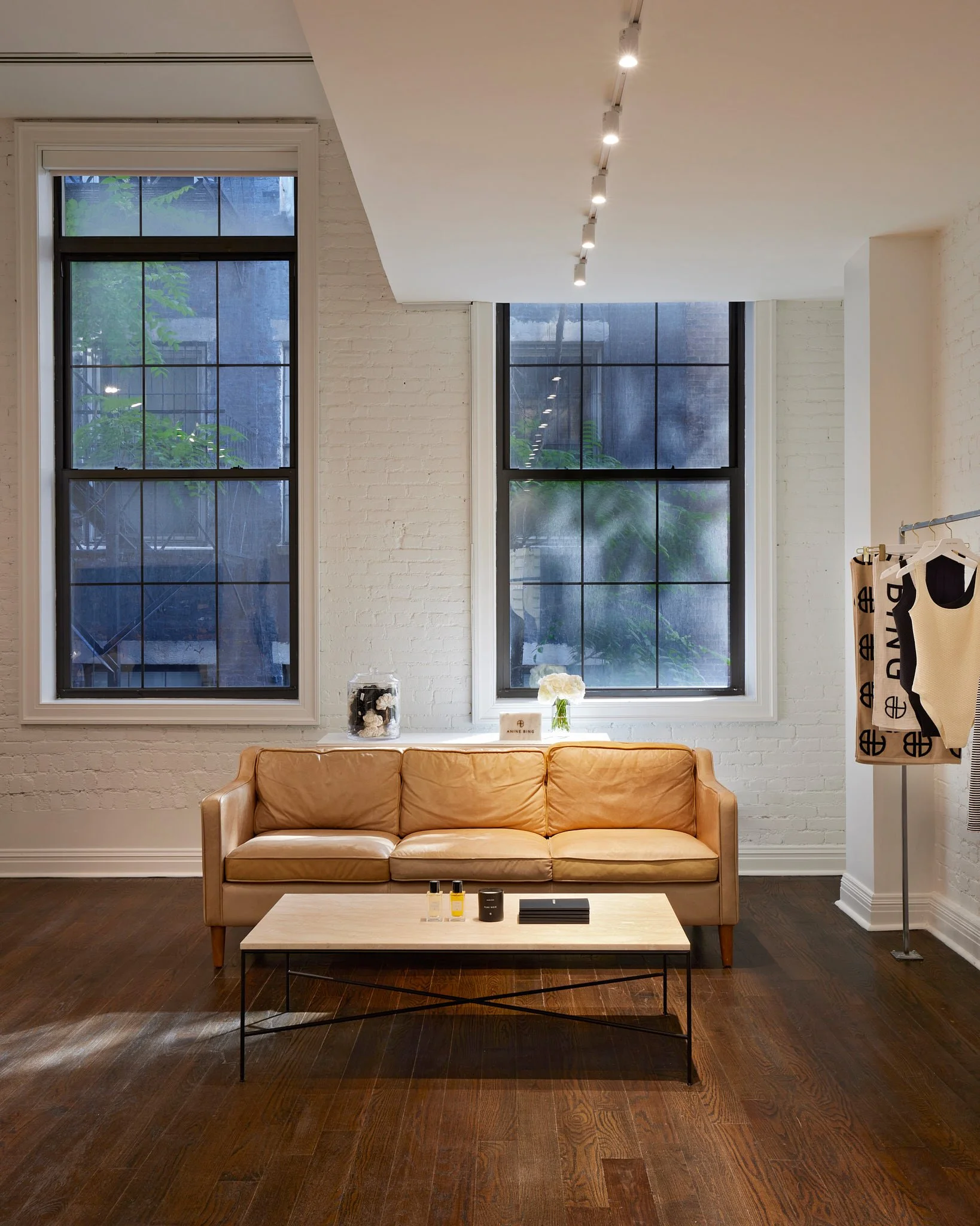 Contemporary retail showroom with a tan leather sofa, large windows, white brick walls, and a modern coffee table.