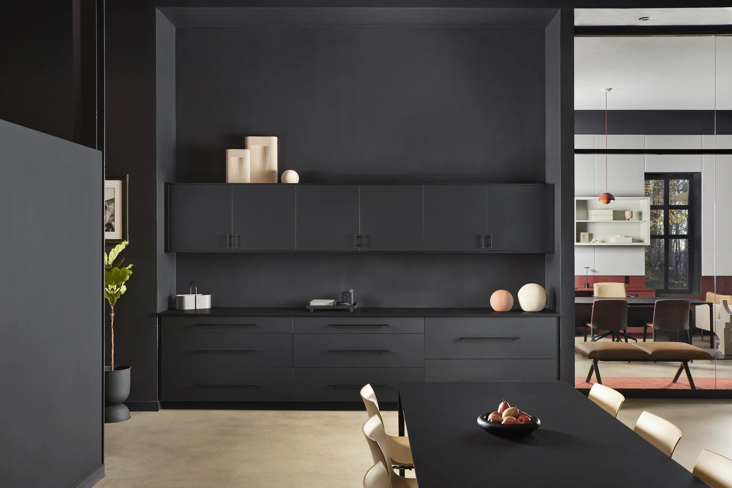 Sleek office kitchen with matte black cabinets, beige flooring, minimalist decor, and modern lighting.