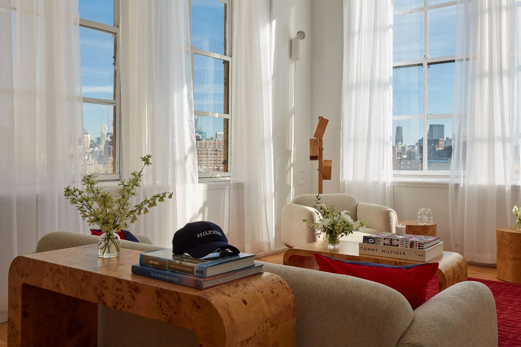 Luxury showroom lounge with burl wood furniture, plush seating, floor-to-ceiling windows, and panoramic city views.