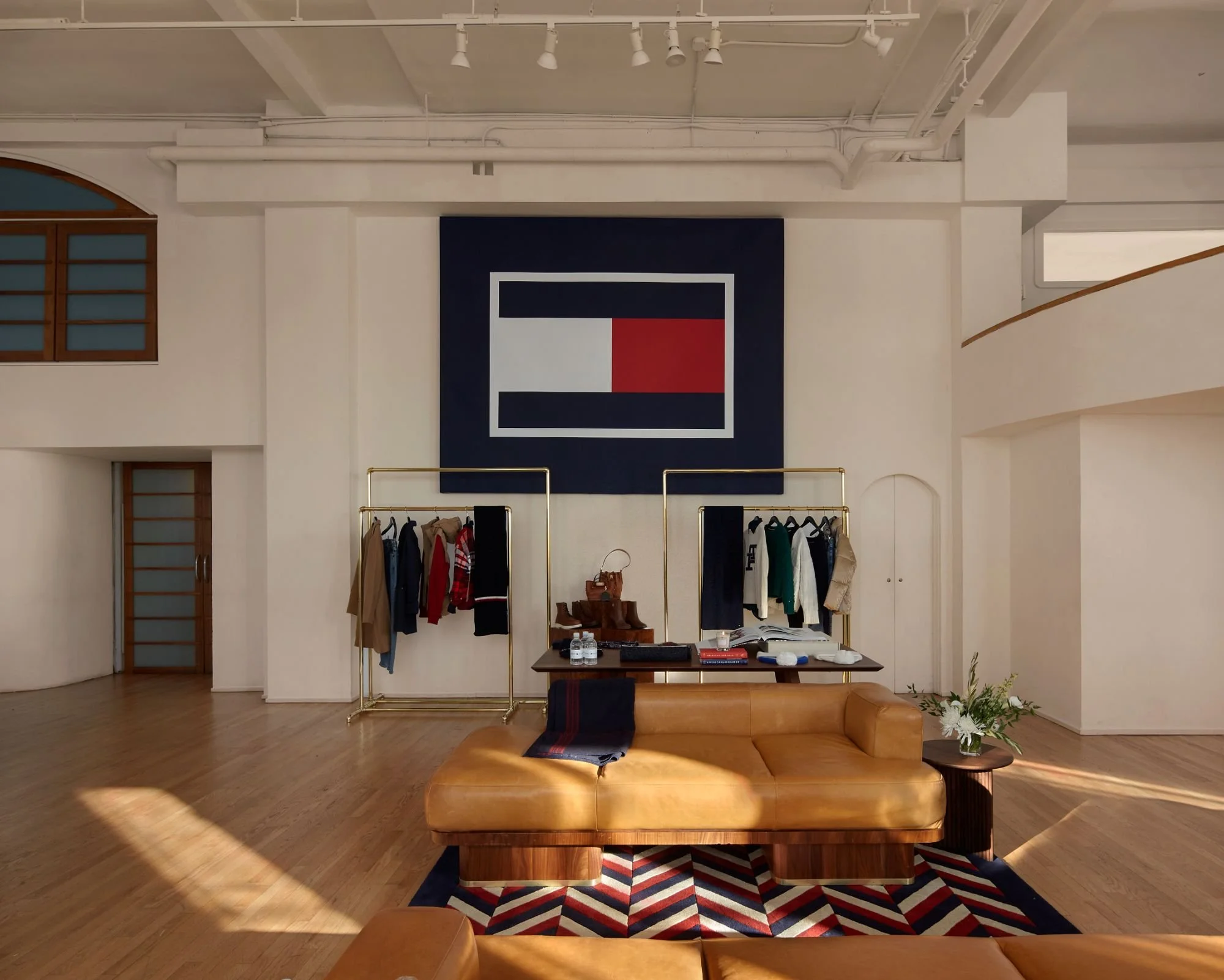 High-end retail showroom with modern furniture, gold clothing racks, a bold graphic wall feature, and natural light.