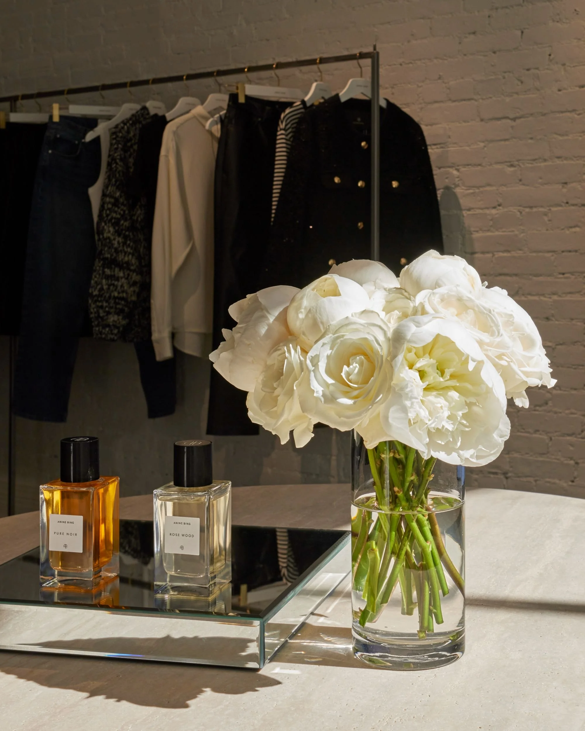 Luxury boutique display with designer perfumes, white roses in a glass vase, and a mirrored tray on a minimalist marble table.