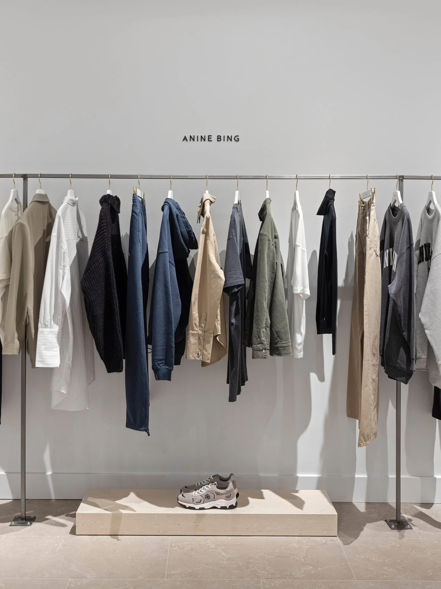 Minimalist retail display with neutral-toned clothing on a metal rack, beige stone platform, and modern boutique styling.