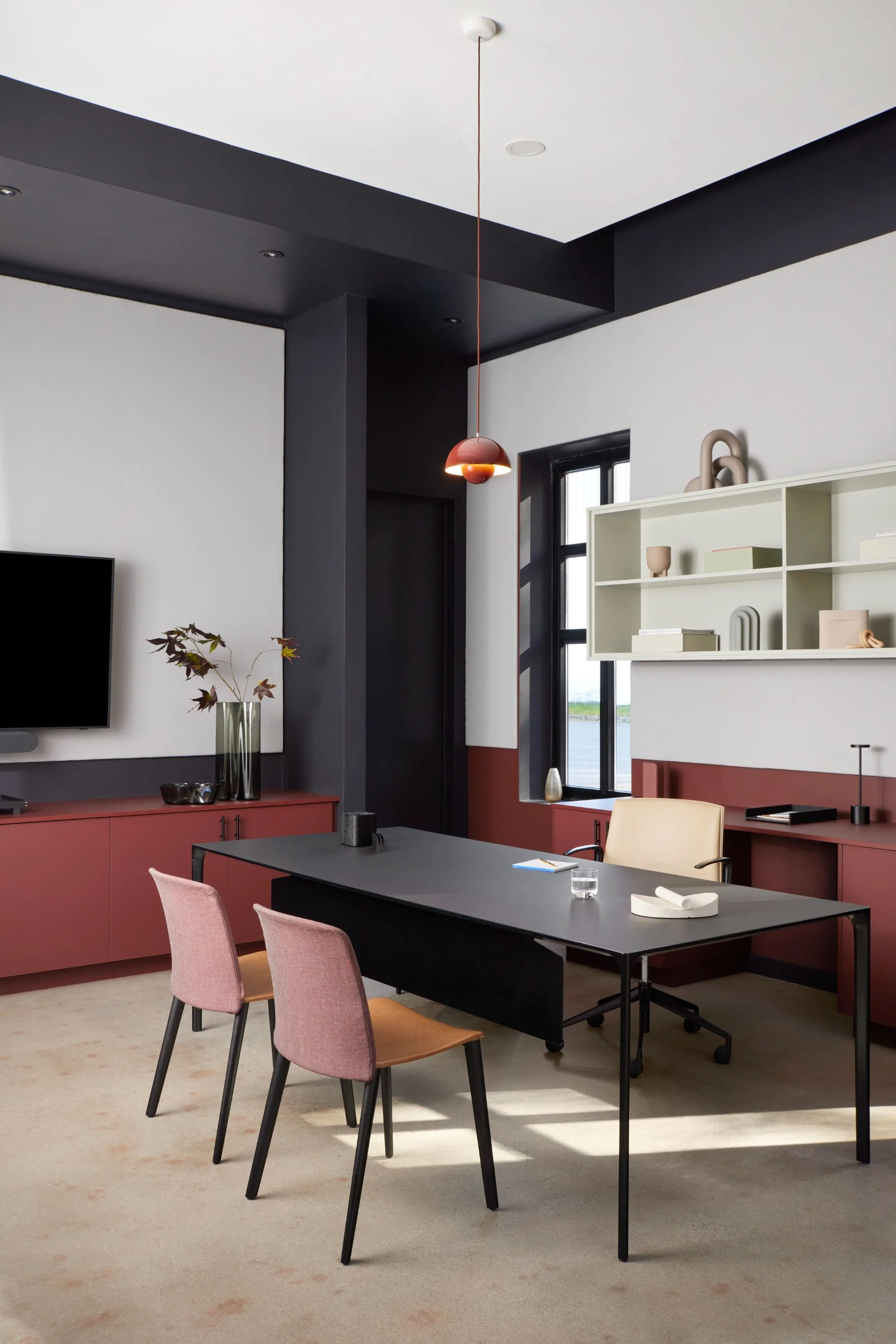 Modern office with deep red and black color-blocked walls, sleek desk, pendant lighting, and minimalist shelving.