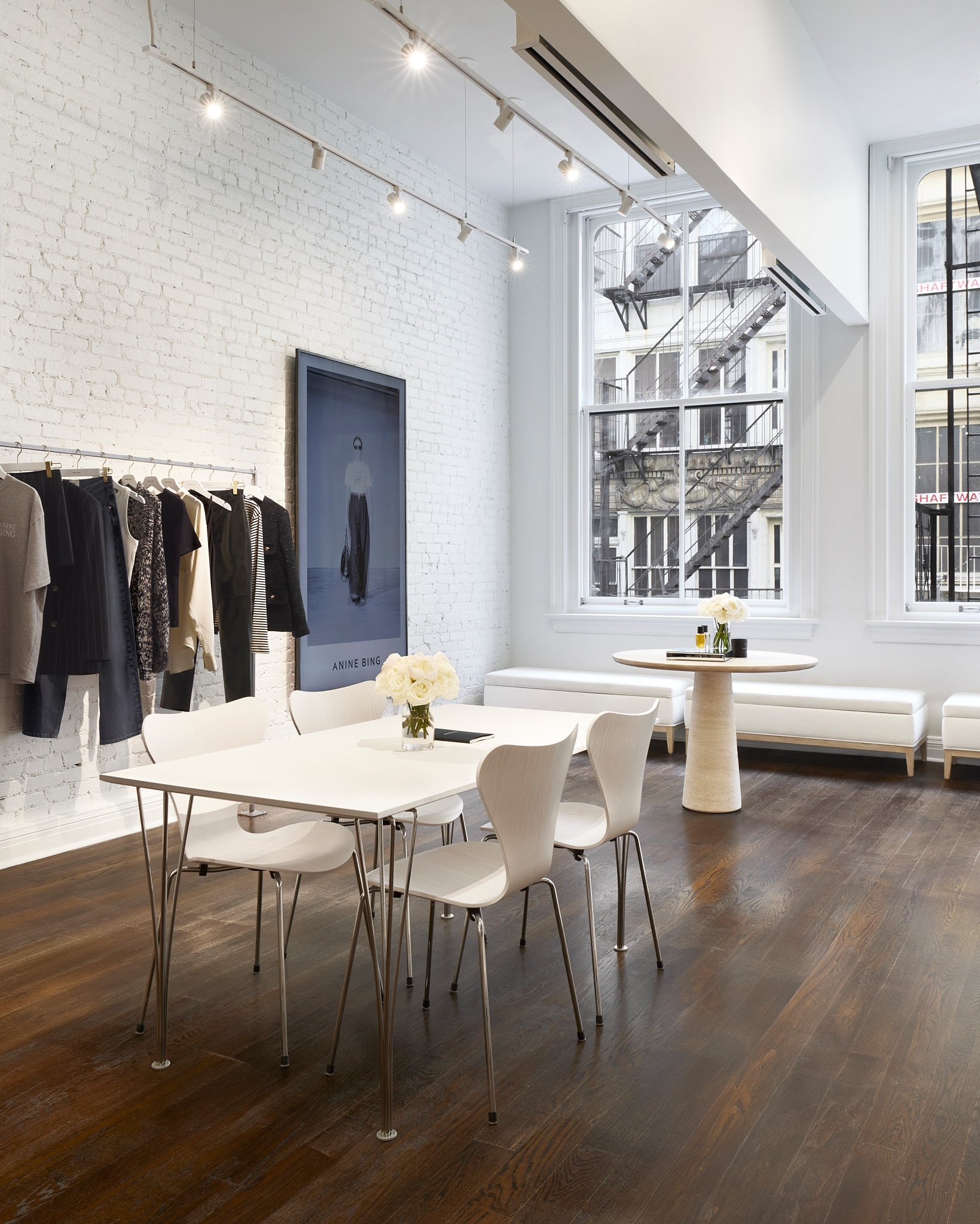 Showroom with white brick walls, minimalist clothing racks, sleek white tables, and large windows overlooking a city street.