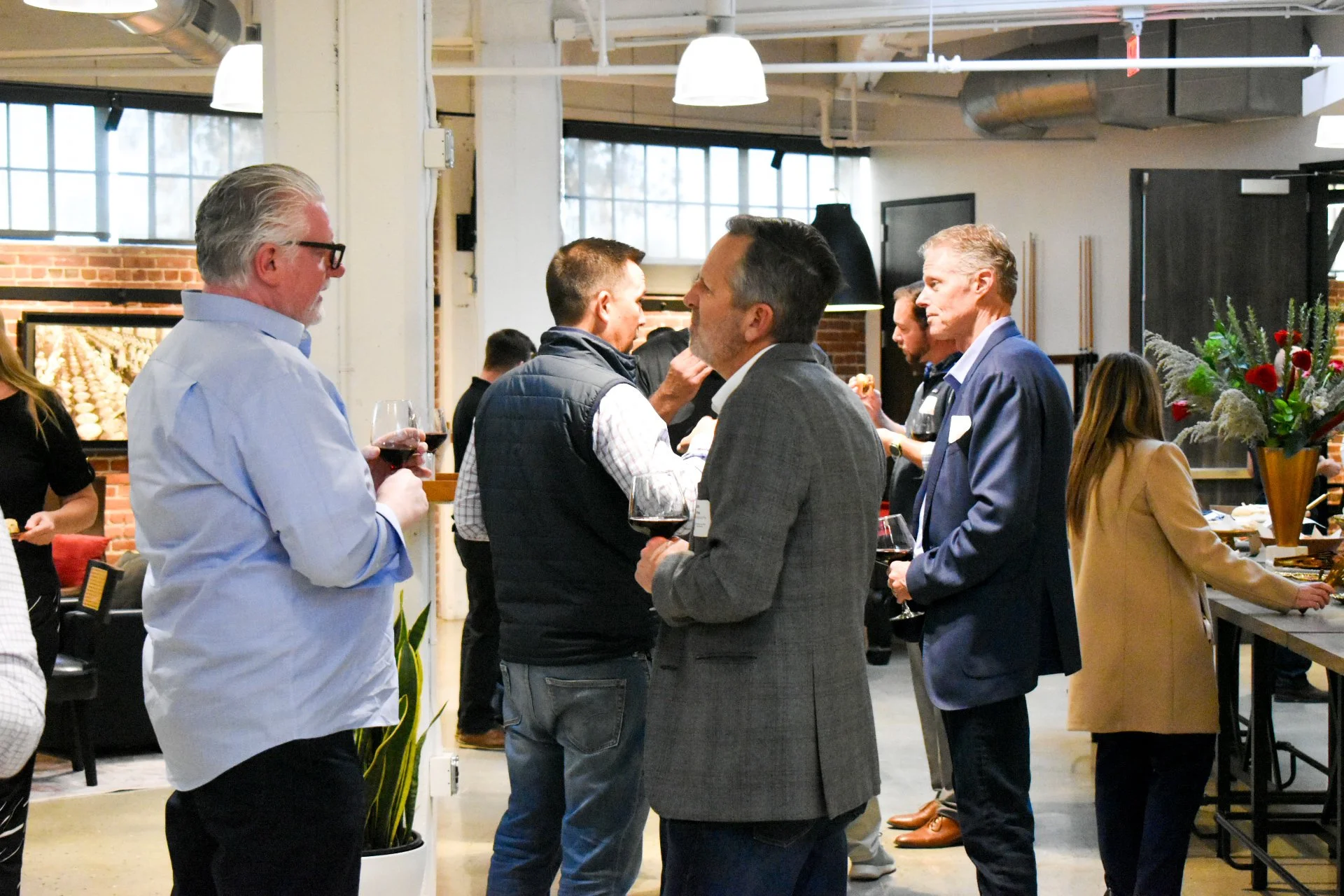 People socializing at a wine-tasting event in a modern indoor space with industrial decor, holding glasses of red wine.