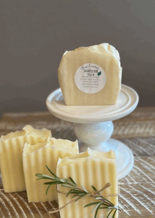 kays-essentials-tallow-shampoo-bar-one-wrapped-on-white-pedestal-three-bars-on-table.jpg