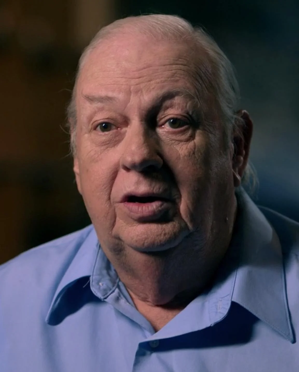Elderly man with white hair wearing a blue shirt.