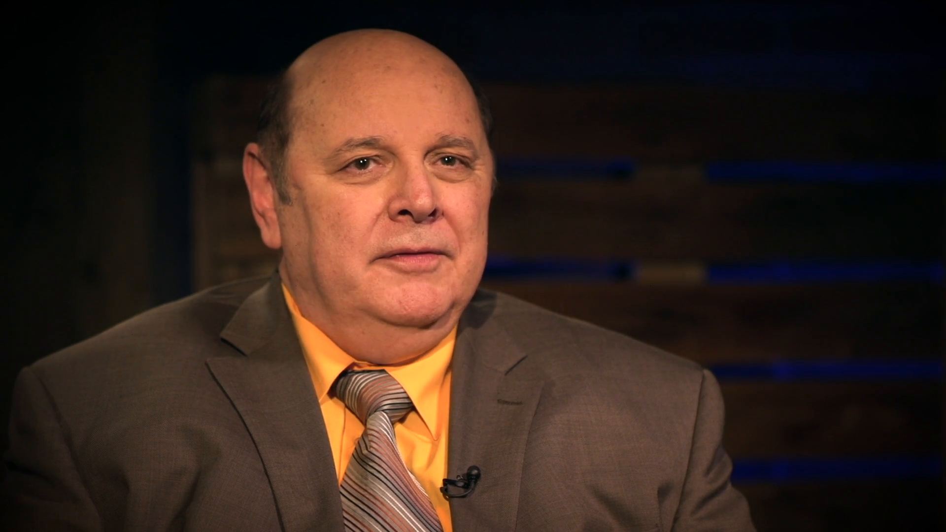 Man in a suit speaking on a talk show set.