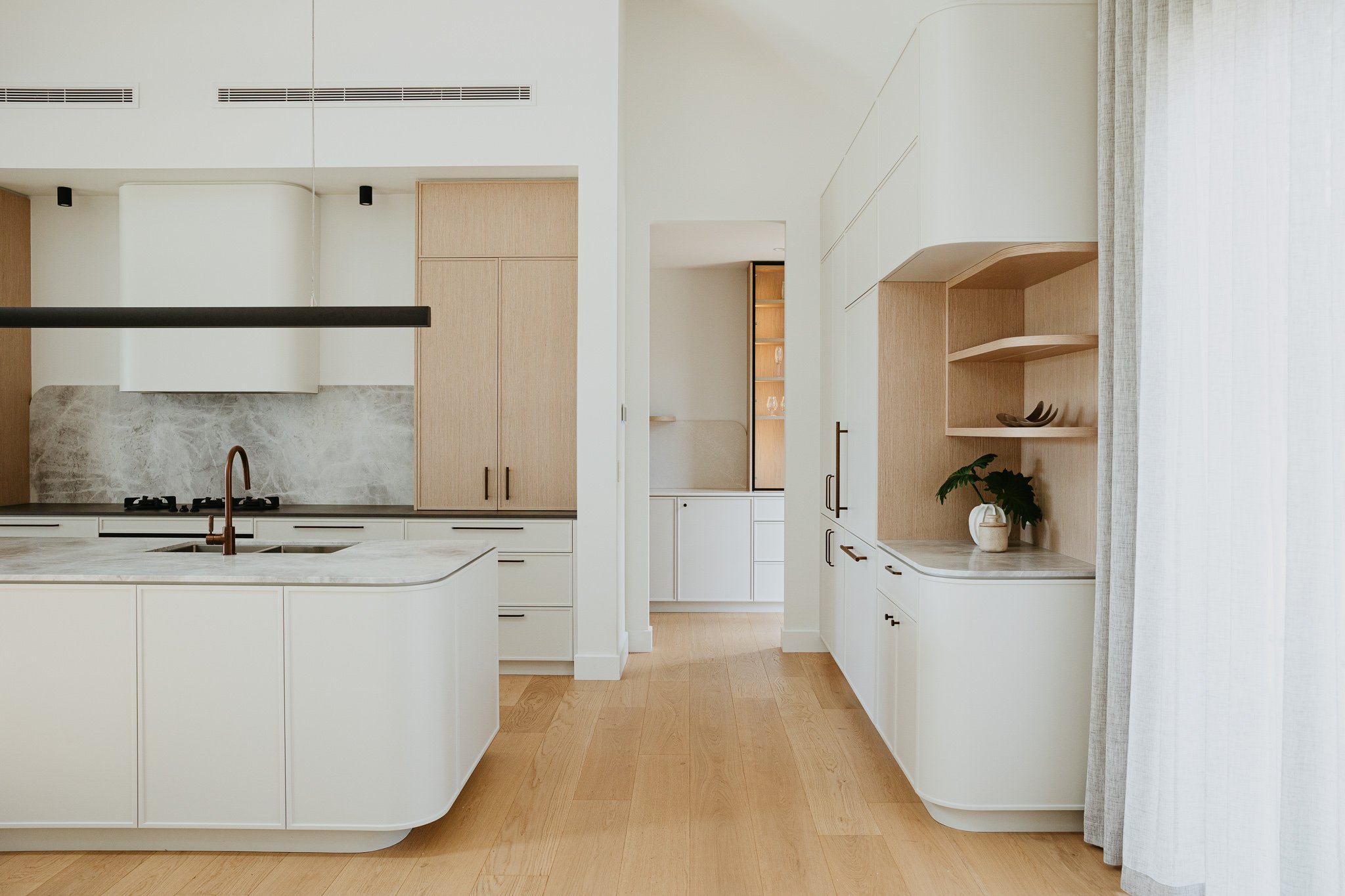 Elegant modern kitchen with a curved island, marble-look splashback, and timber cabinetry, creating a sophisticated yet practical entertaining space.