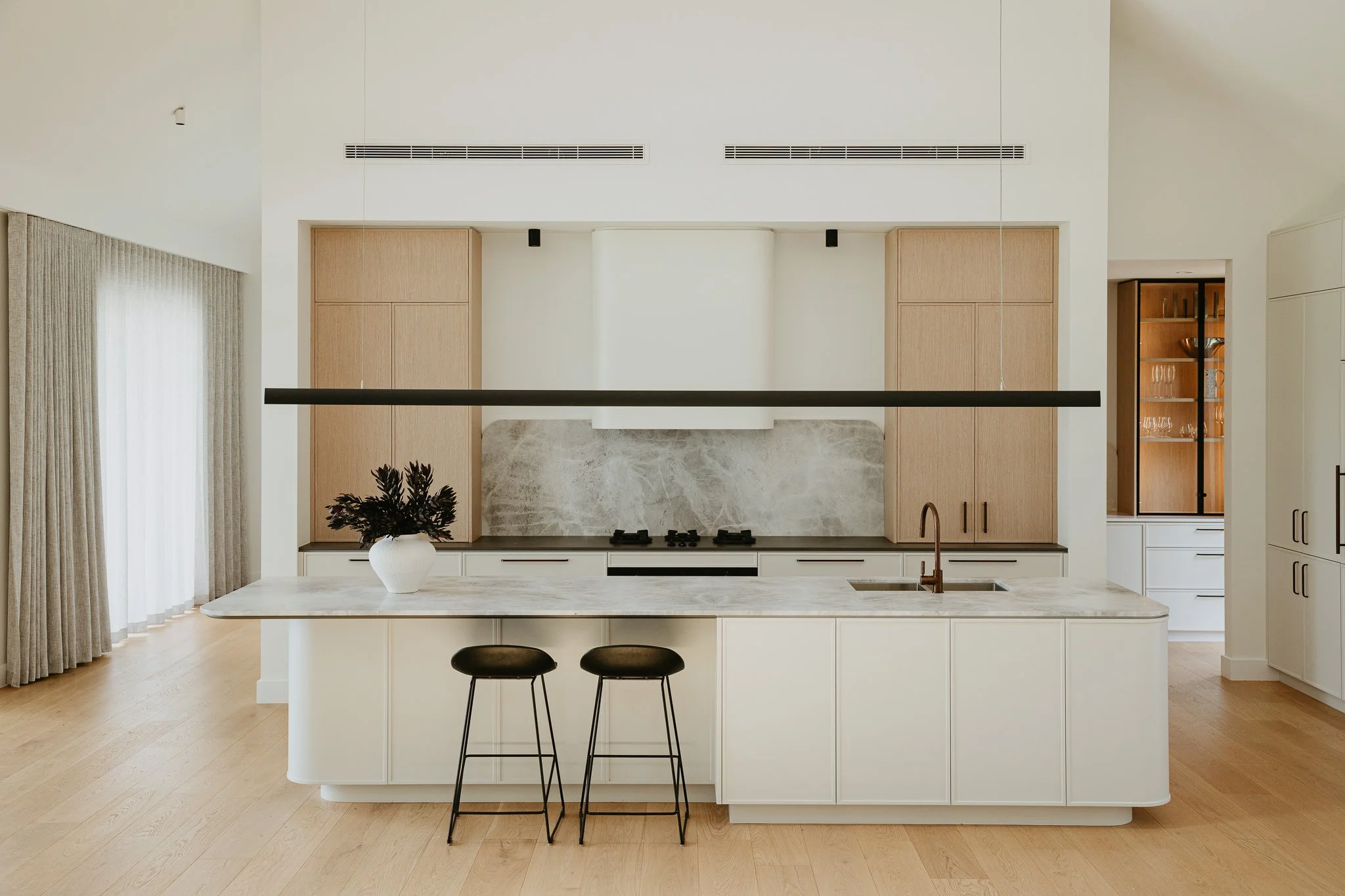 Modern minimalist kitchen with a large curved island bench, natural timber cabinetry, and soft neutral tones, designed for luxury family living in Australian homes.