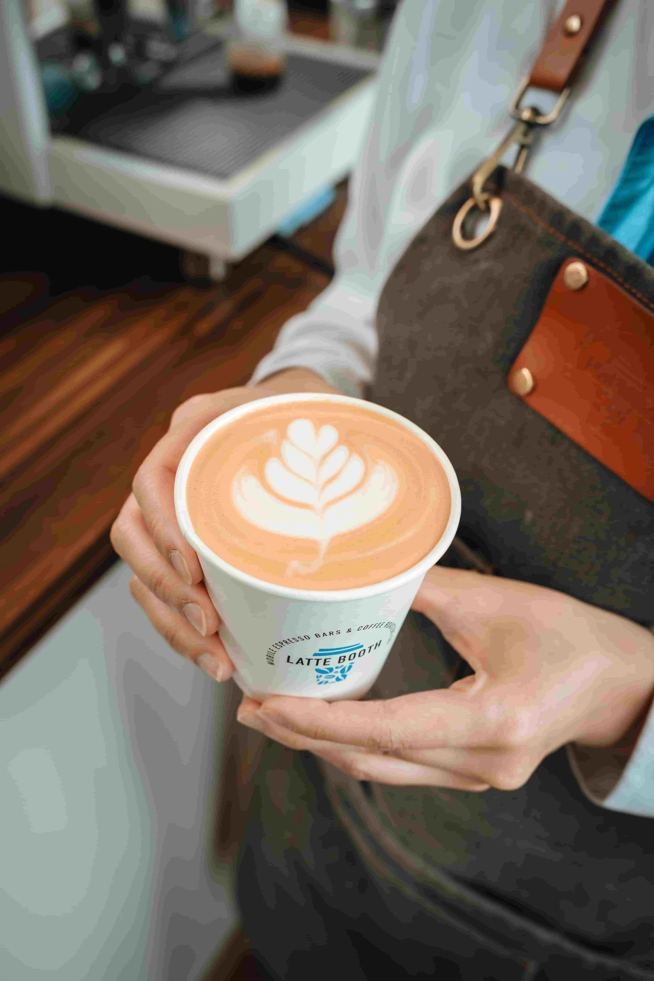 Paper cup with Latte Booth Logo is being presented by a barista with a tulip Latte Art