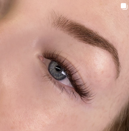 Close-up of a person's eye with long eyelashes and defined eyebrow.