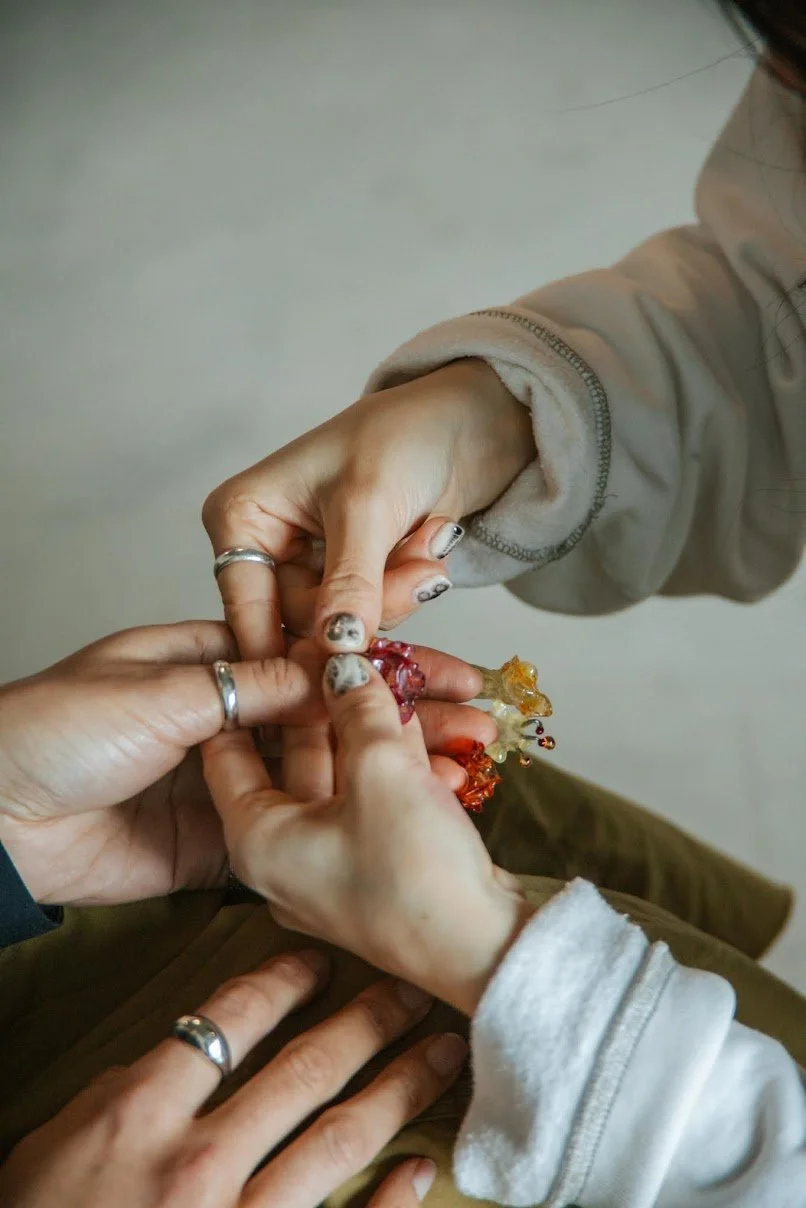 Three hands with rings interacting, holding colorful objects.