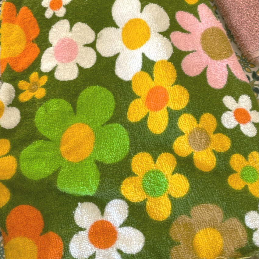 Close-up of a colorful floral towel with various flowers in white, yellow, pink, orange, and green on a green background.