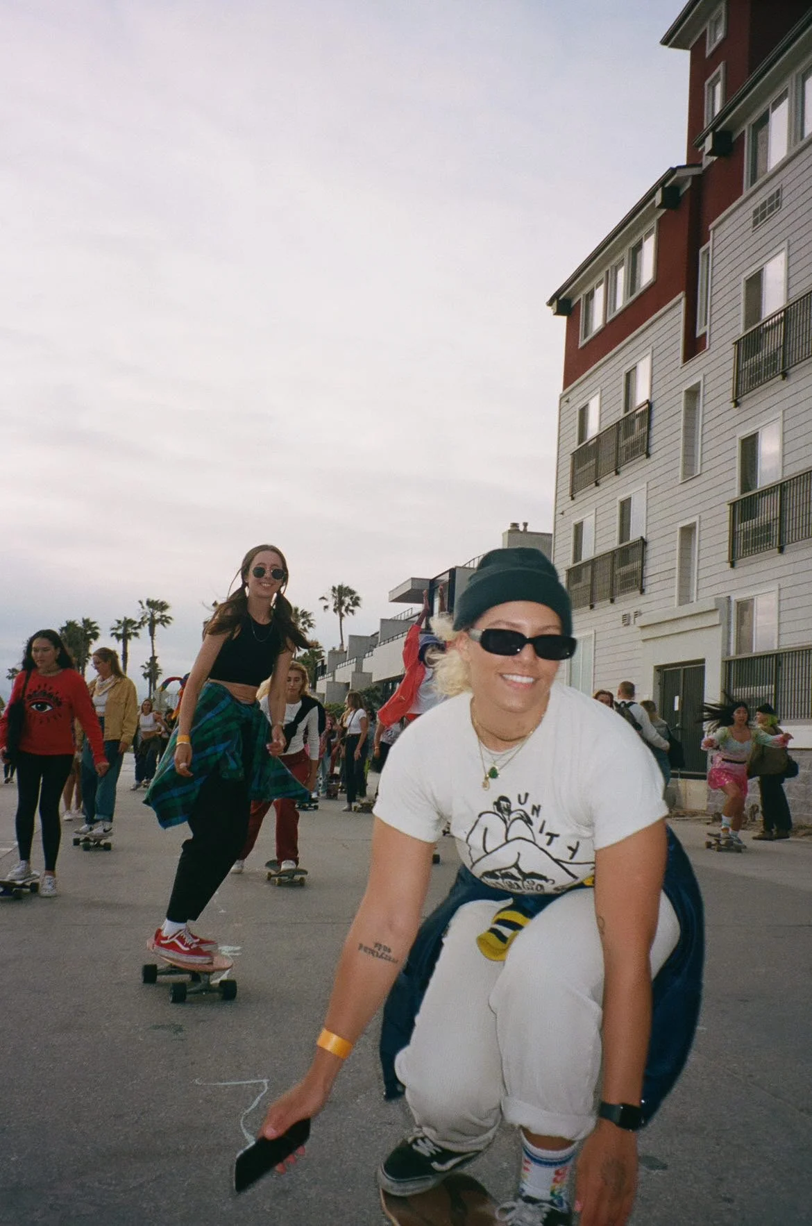 People skateboarding outdoors near a residential building, with palm trees in the background.