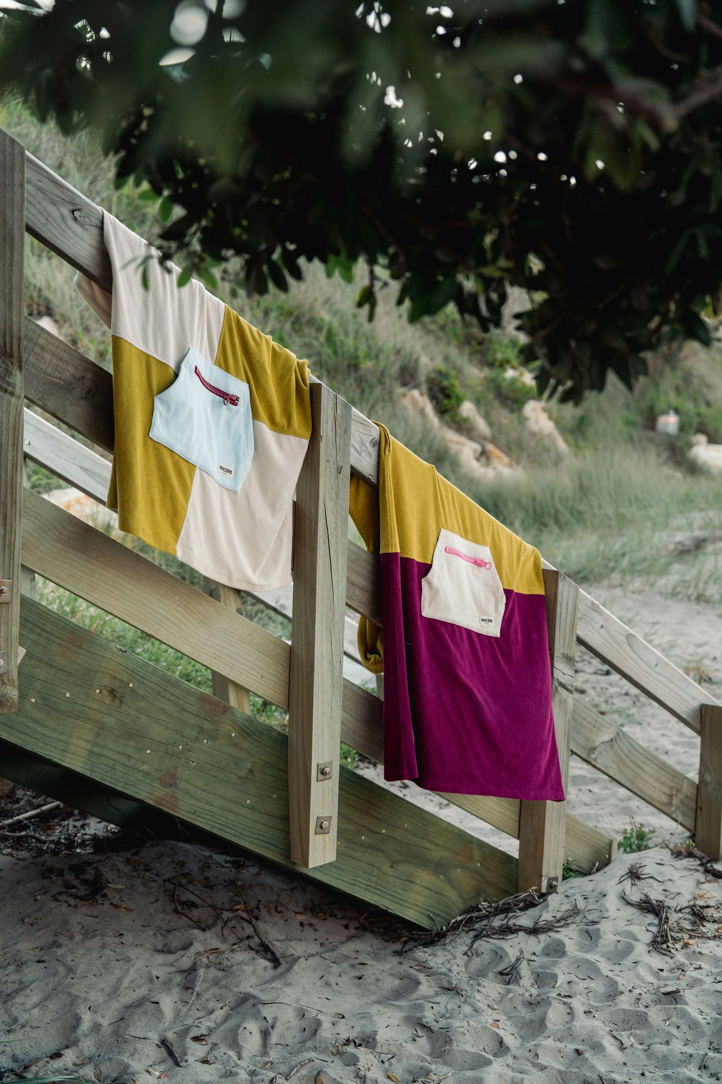 Two WaveyDrip towel ponchos hanging on wooden beach fence