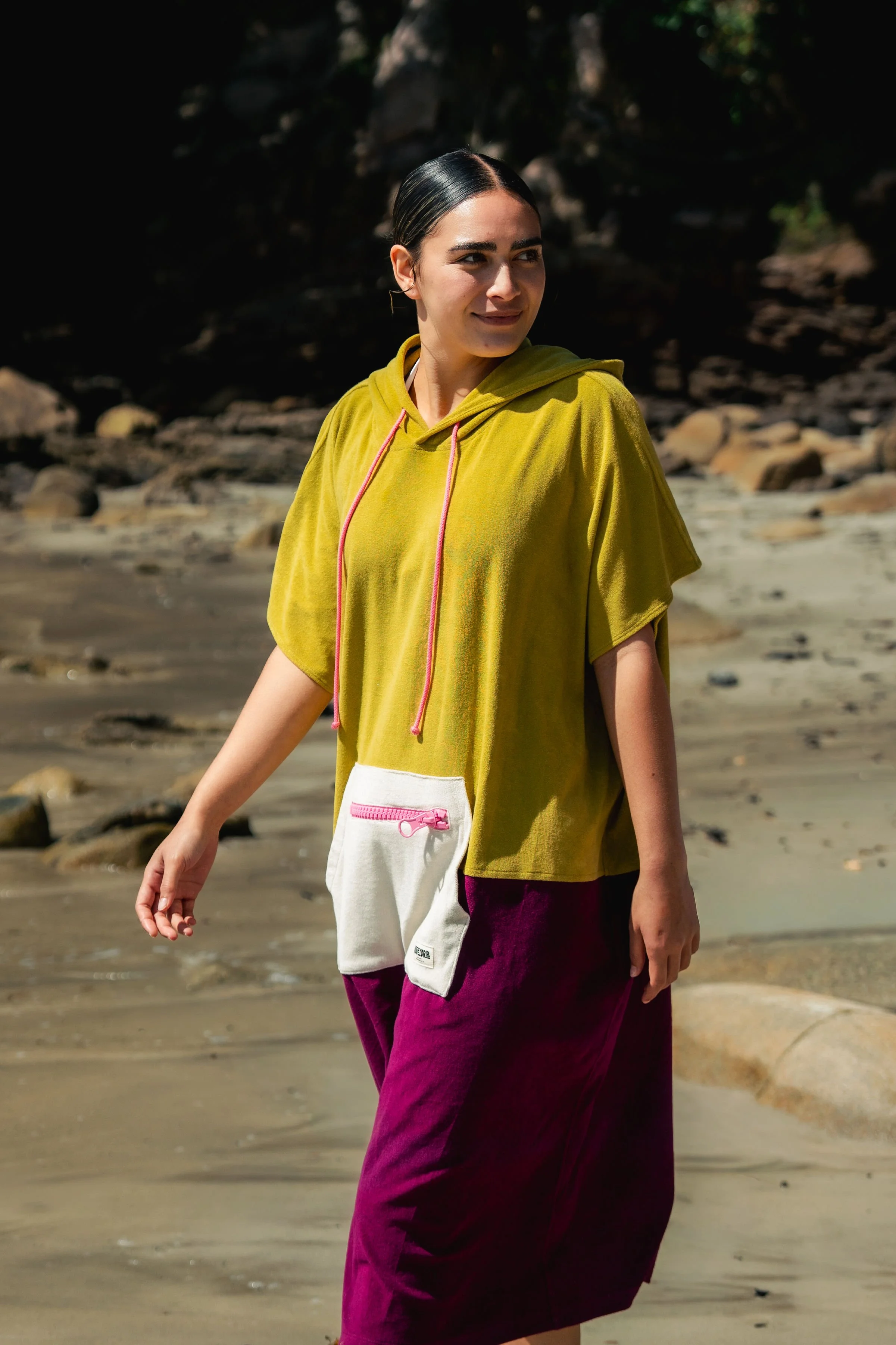 Woman walking on the beach wearing a yellow hoodie, white and pink pouch on her pants, and maroon pants.