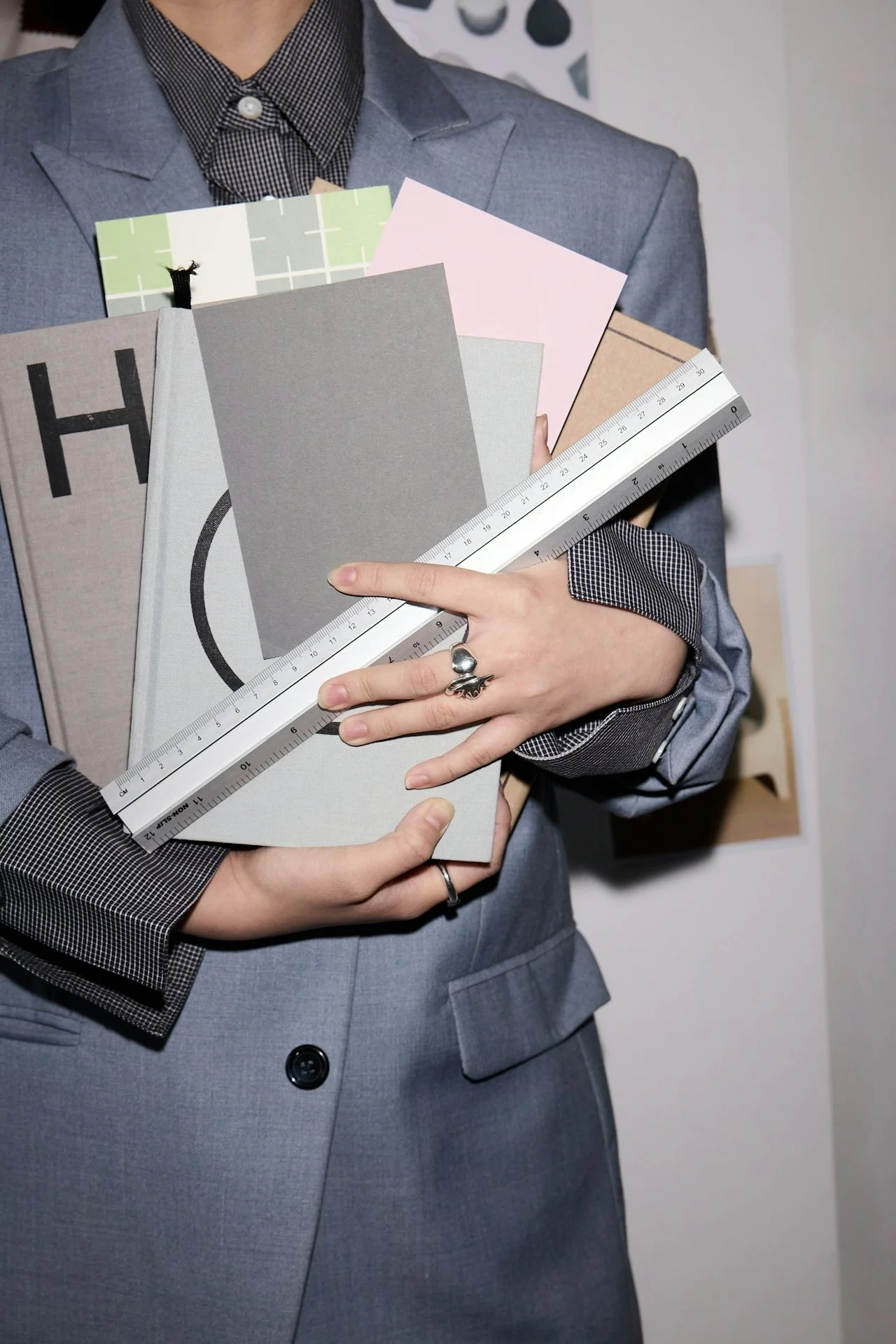 Person wearing a suit jacket holding several books and a metal ruler.