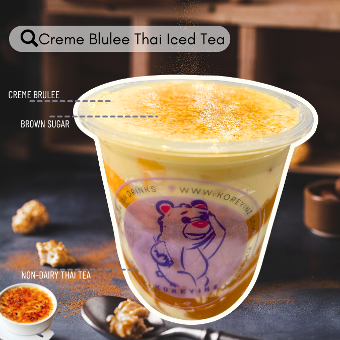 A cup of Creme Bluree Thai iced tea with a layer of caramelized sugar on top, labeled as 'Creme Bluree Thai Iced Tea' with steam rising from the drink, served in a plastic cup that has a bear logo and website, placed on a table with scattered popcorn