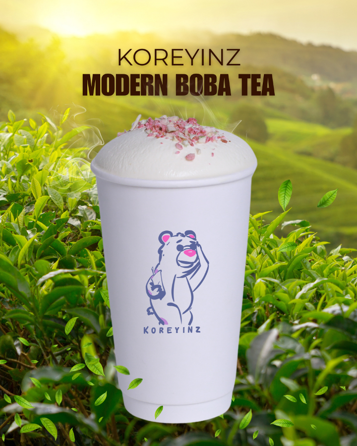 A cup of modern boba tea with pink toppings, featuring a cute cartoon bear logo and the brand name 'KOREYINZ', set against a lush green tea plantation with rolling hills in the background.