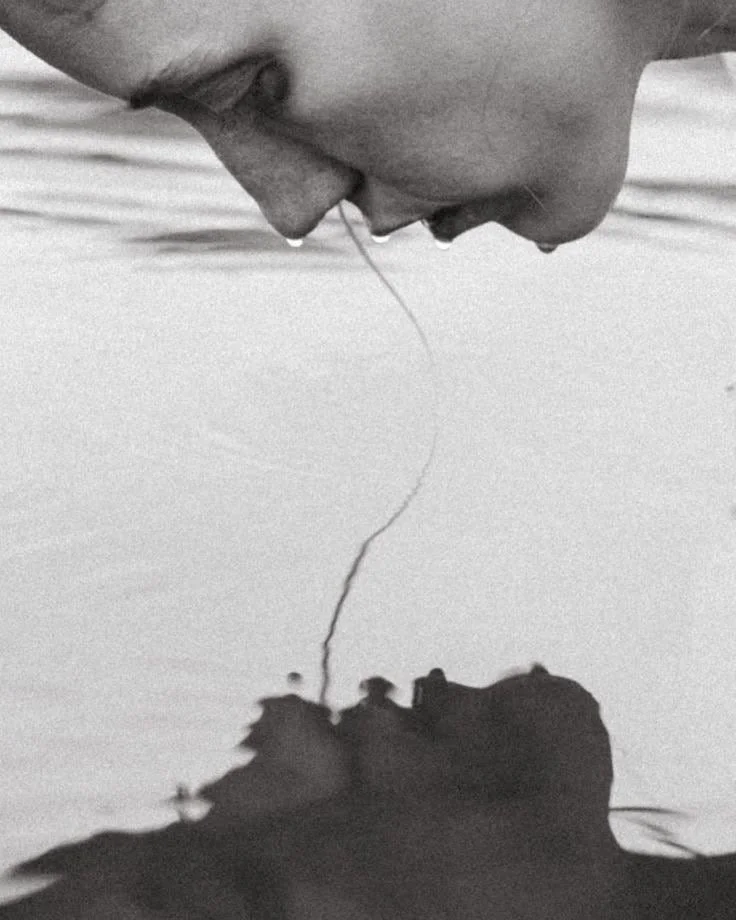 A close-up of a person holding a thin, long object, with their face close to a reflective surface, possibly water, creating a mirrored effect.