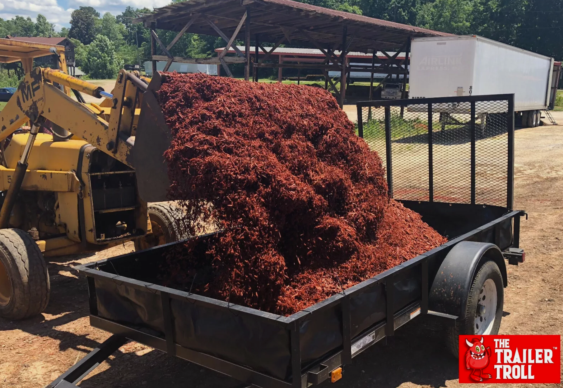 Action shot of a large volume of red mulch being loaded into a utility trailer with the Trailer Troll liner installed. The liner's added height maximizes the trailer's ability to hold bulk landscaping materials