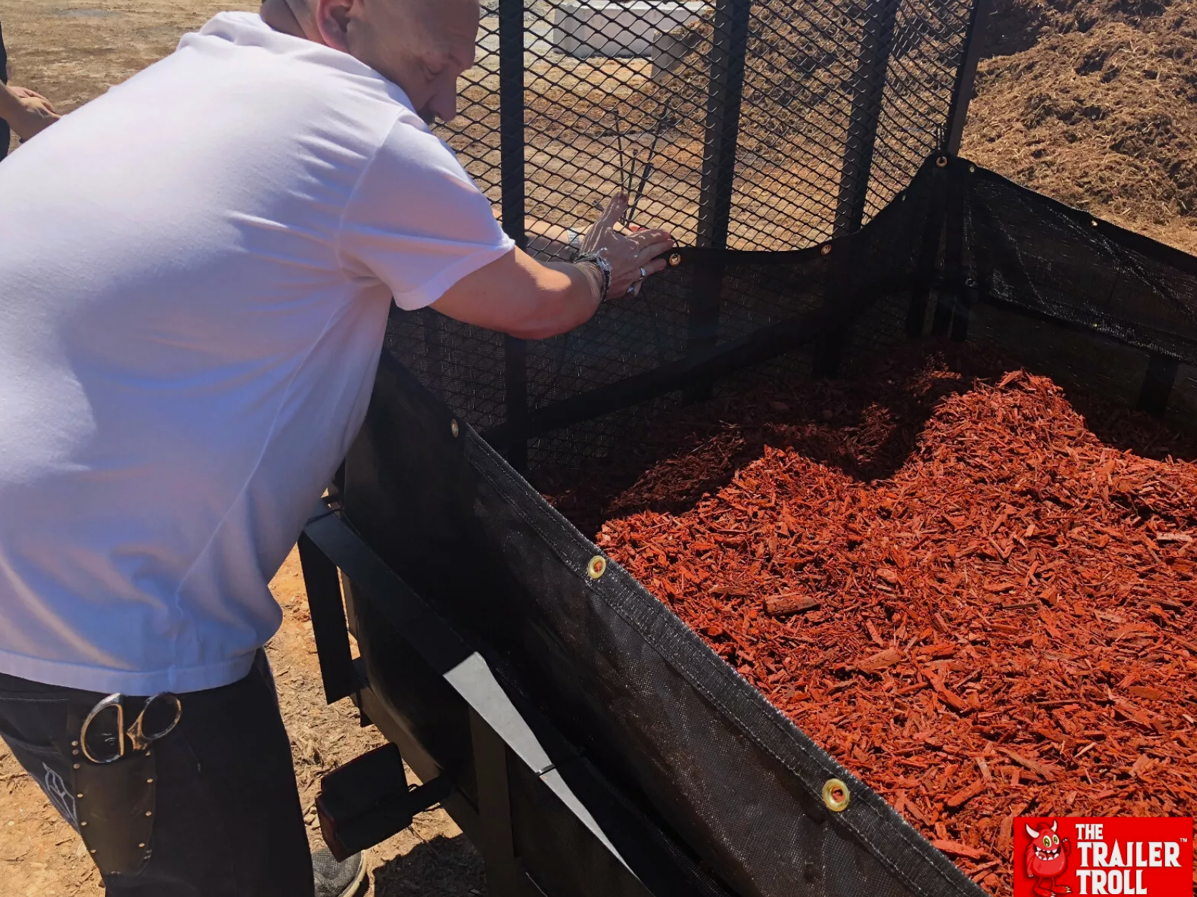 Securing the trailer load with a mesh debris tarp, ensuring the red mulch is fully covered for safe transit