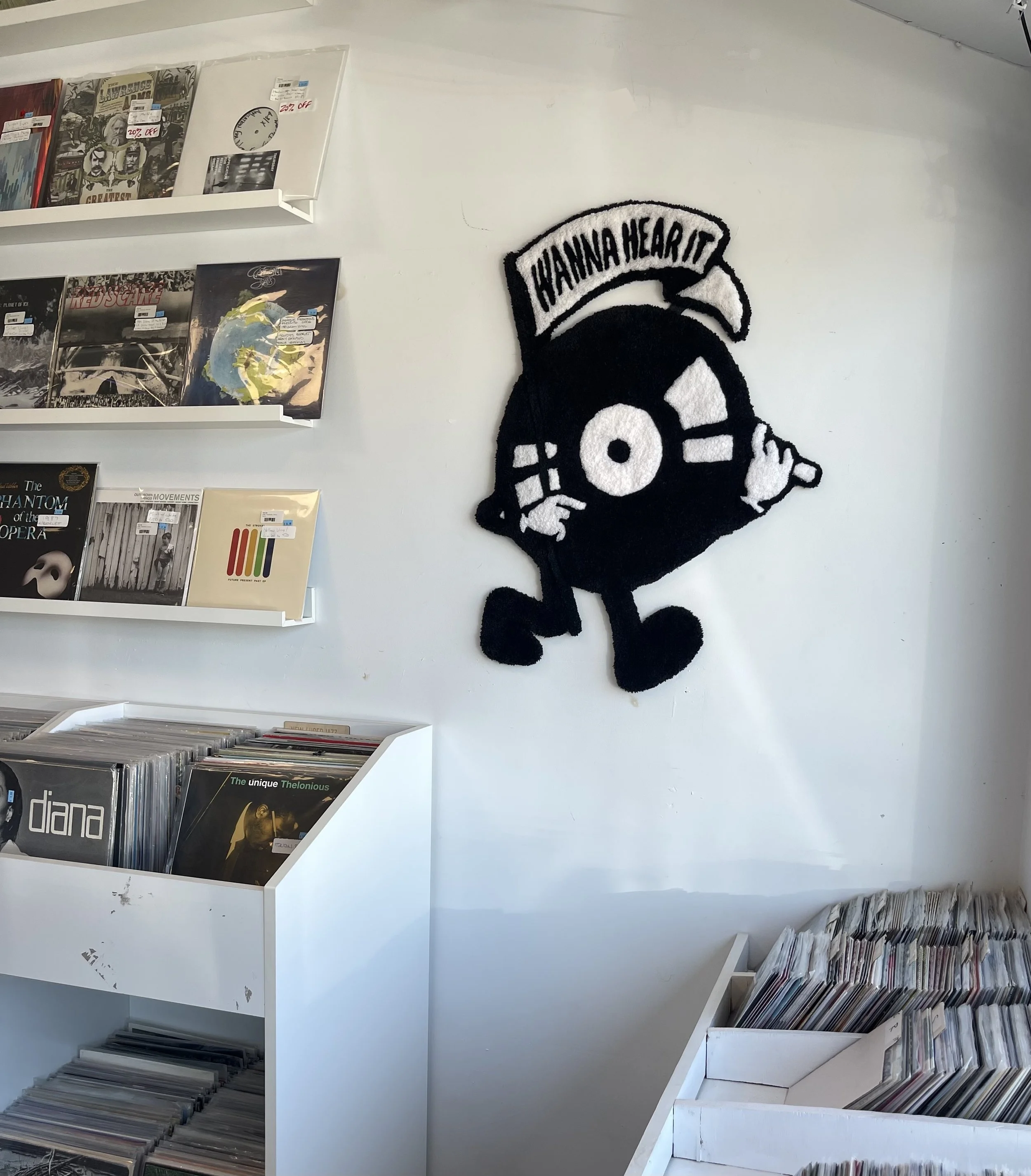 Cutstom store logo: Vinyl records in a store with a cartoon record character on the wall, labeled "WANNA HEAR IT."