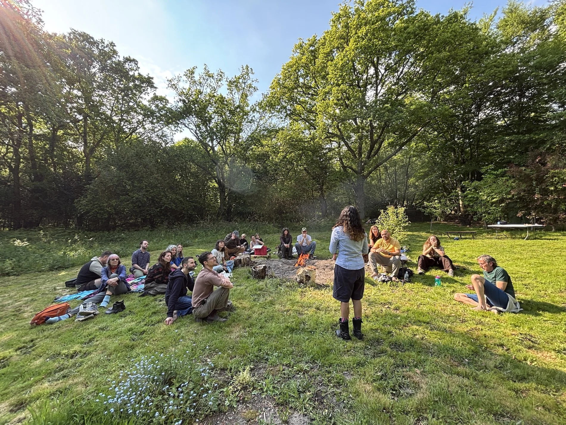Participants sit in a meadow around a campfire as Sana Jazeer shares a decomposition story.