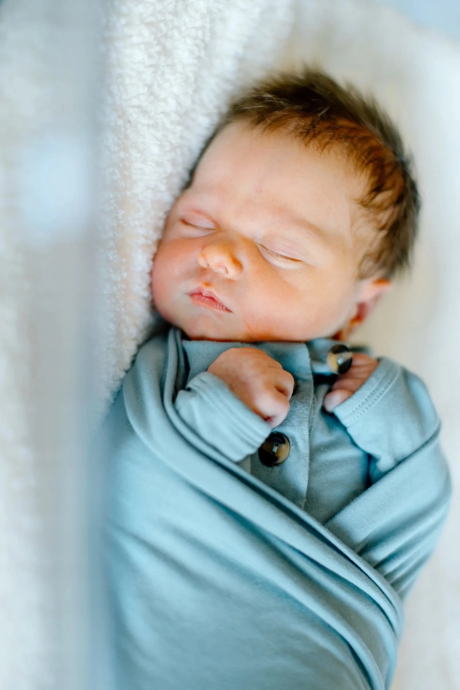 A sleeping newborn baby wrapped in a blue blanket, lying on a soft surface.