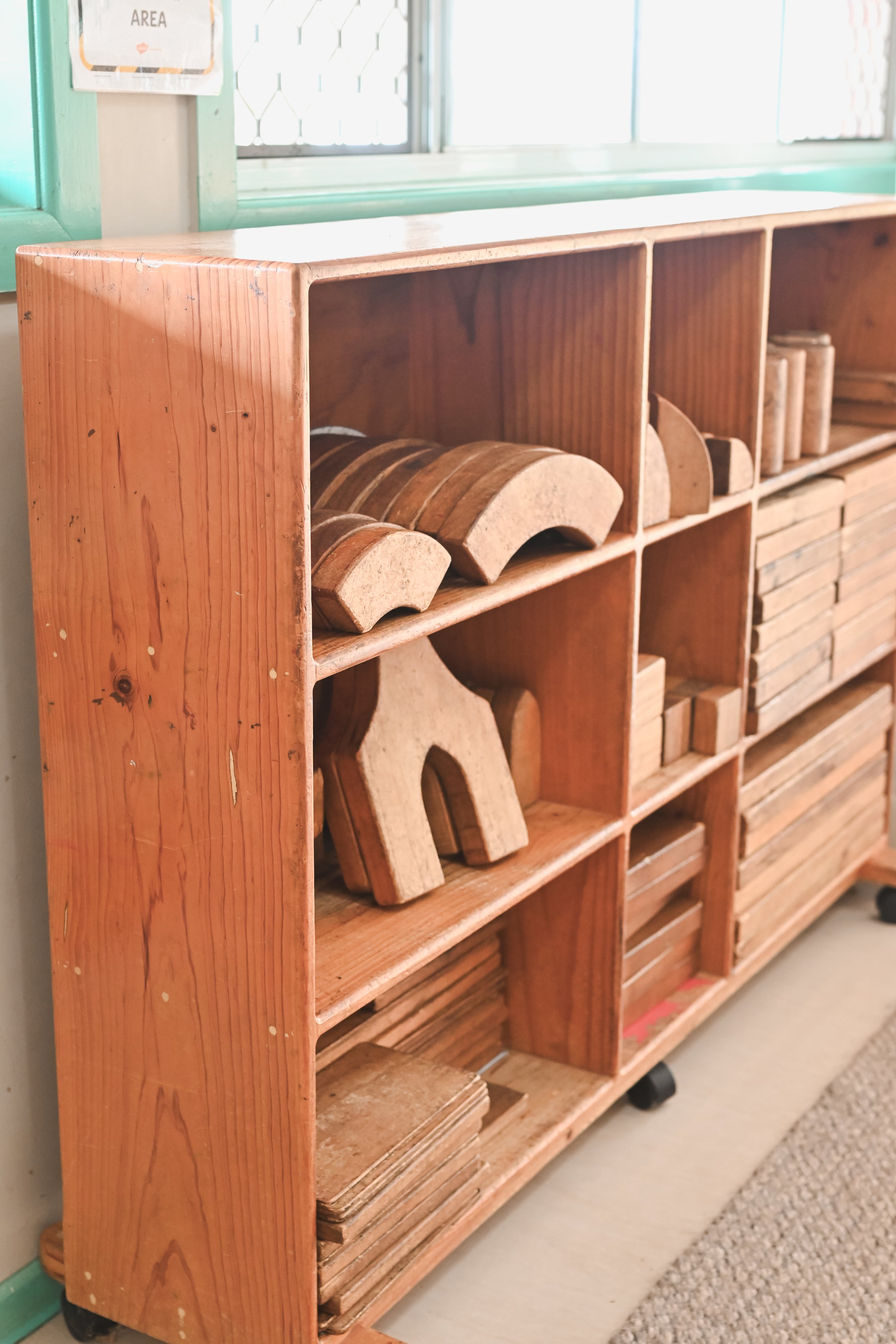 Wooden shelf with various wooden blocks and shapes for building or play.