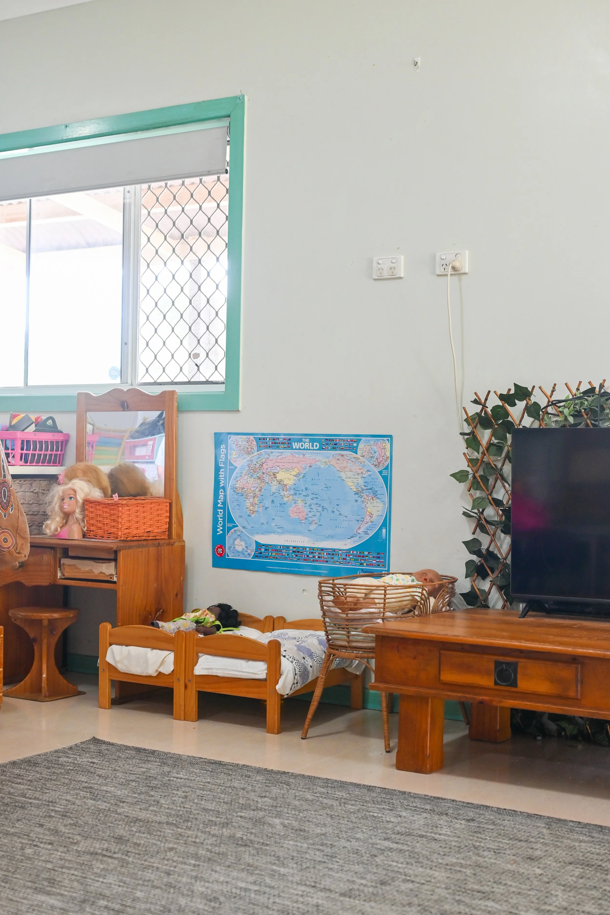 Indoor playroom with world map, dollhouse furniture, TV, and plants.