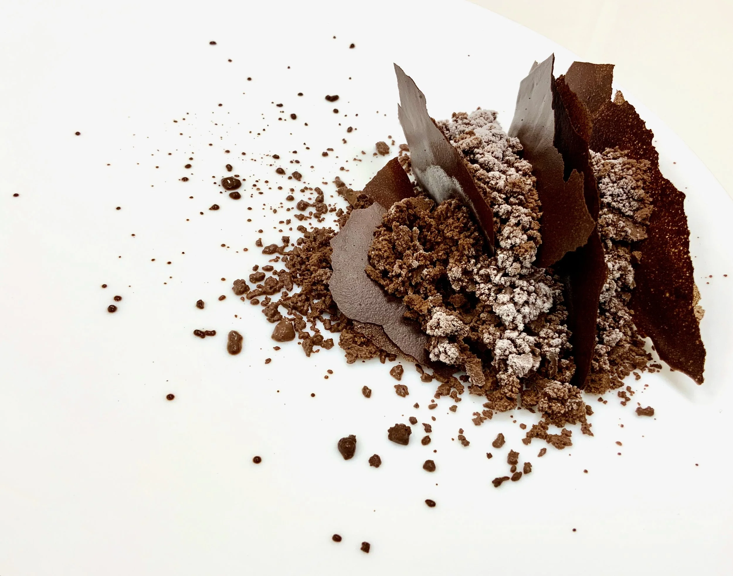 Bean-to-bar chocolate textures by Chris Quirós — gourmet dessert with cocoa shards, soil, and creamy elements plated artistically on a white dish.