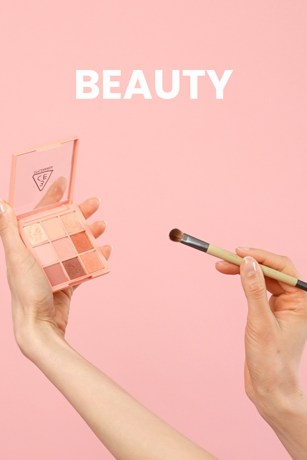hands hold a makeup brush and a pink eyeshadow palette in front of a pink backdrop