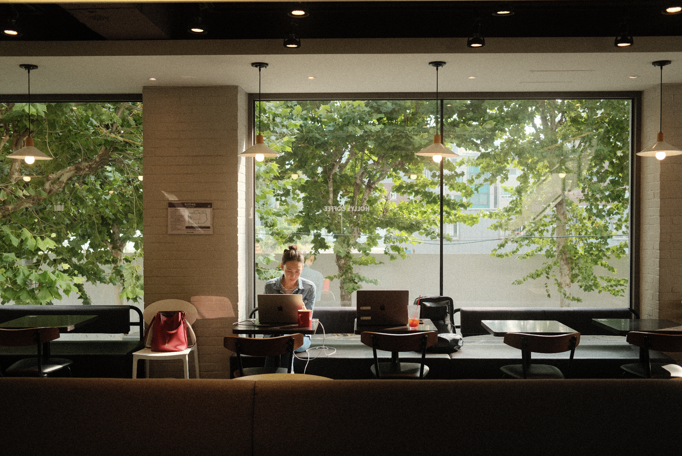 Rebecca Rose wears a jean jacket while sitting at a cafe as sunlight streams through the windows