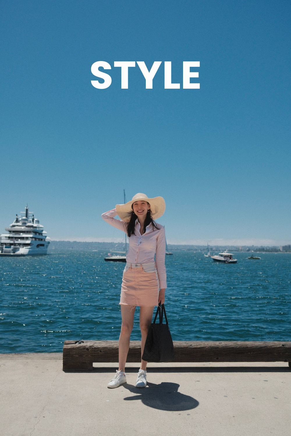 A beautiful woman wearing a sun hat and a pink mini skirt stands in front of a blue ocean