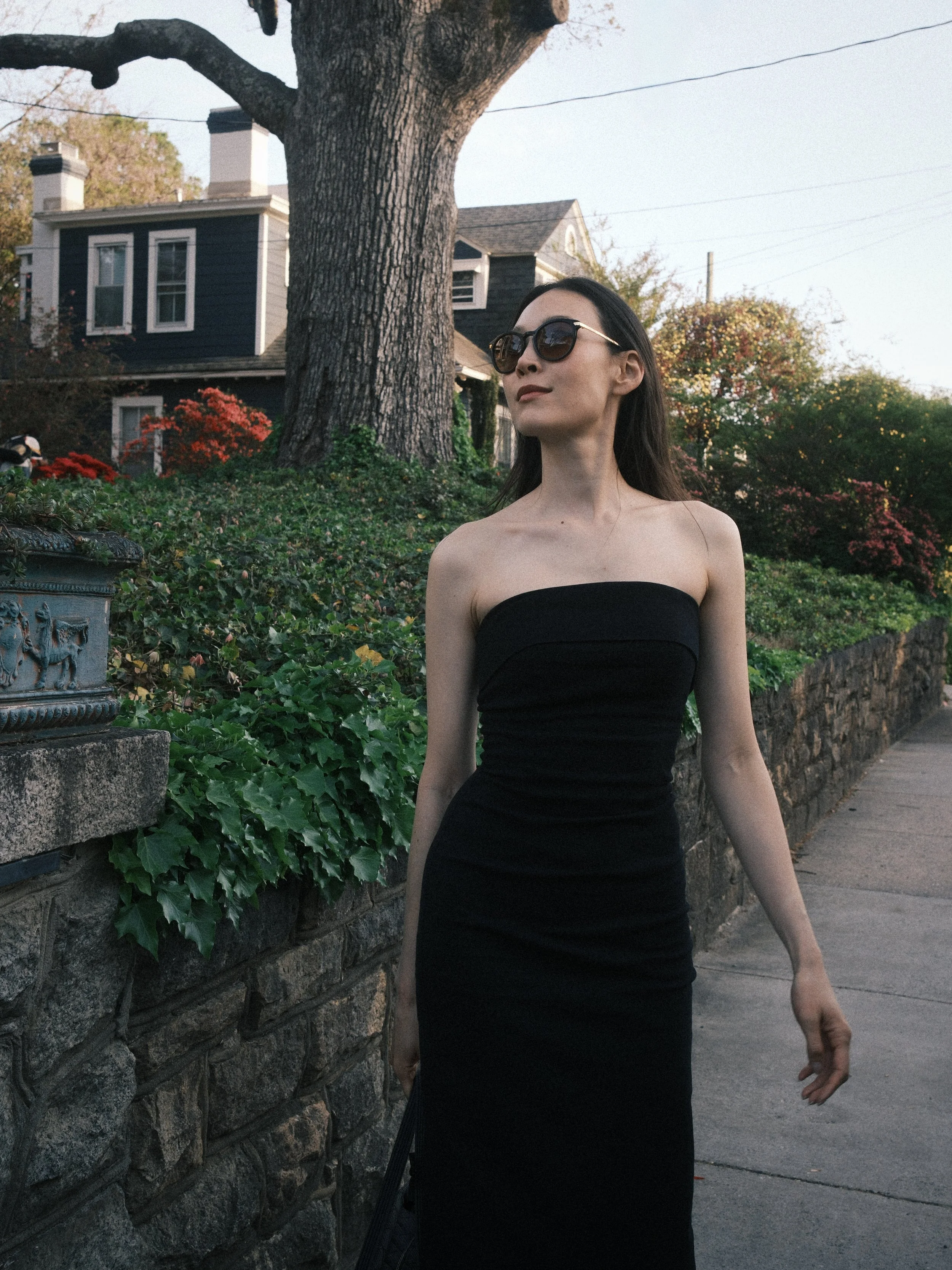 A beautiful woman wears a tight, strapless black dress and sunglasses