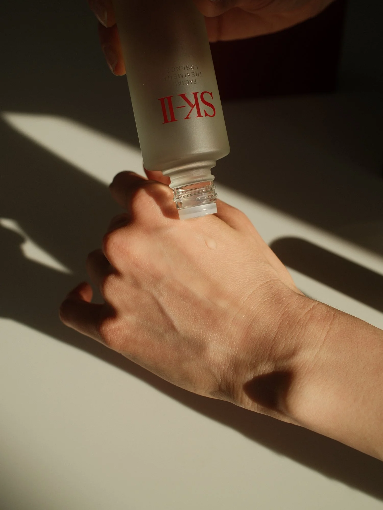 A hand holds the SK-II Facial Treatment Essence bottle and pours a small drop on the back of another hand.