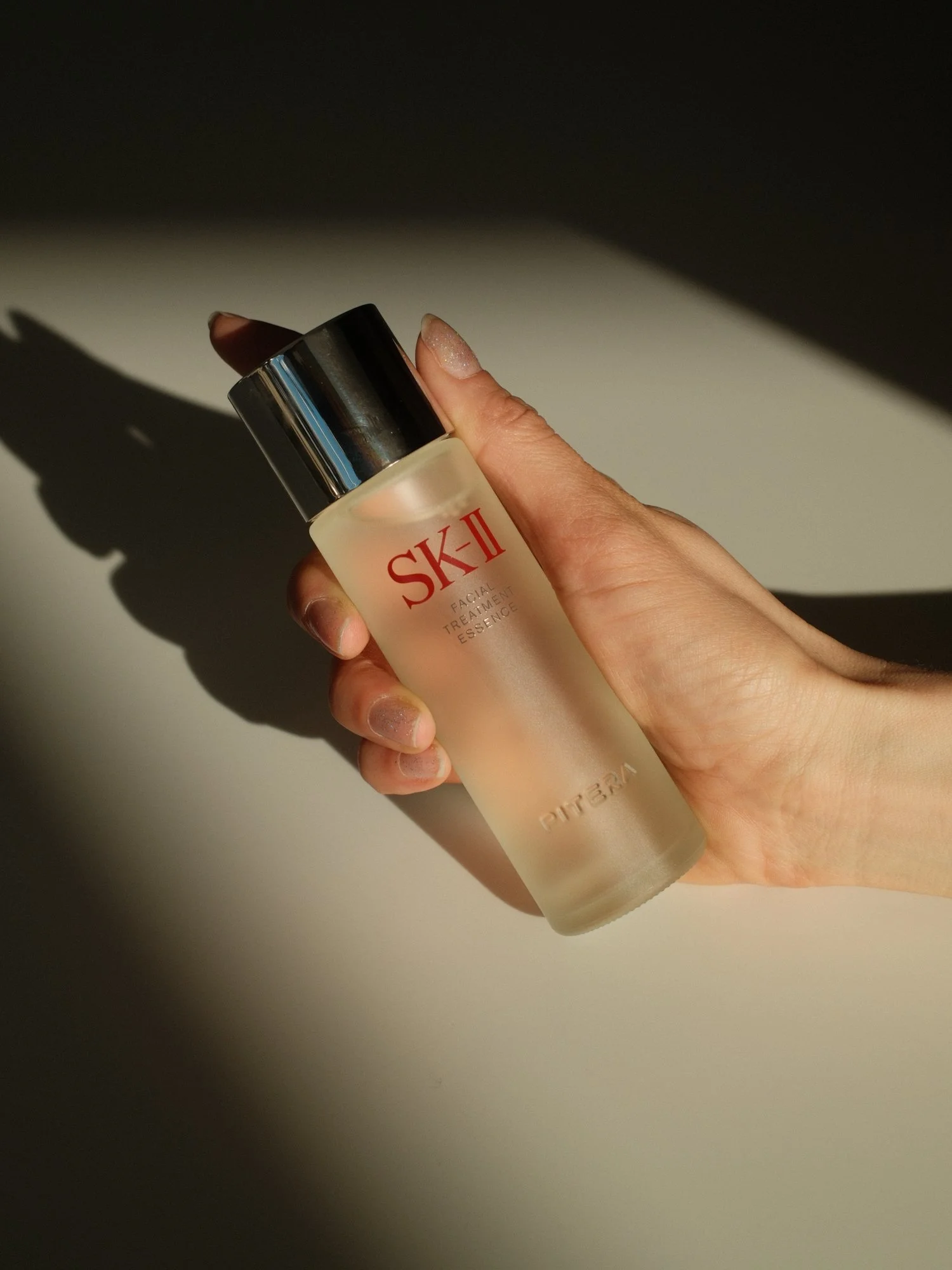 A slim hand holds an SK-II facial treatment essence bottle, while the sun hits it and makes the bottle glow