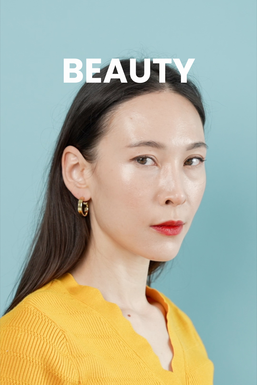 A Korean model is wearing a yellow shirt and gold hoop earrings and is staring at the camera against a blue backdrop