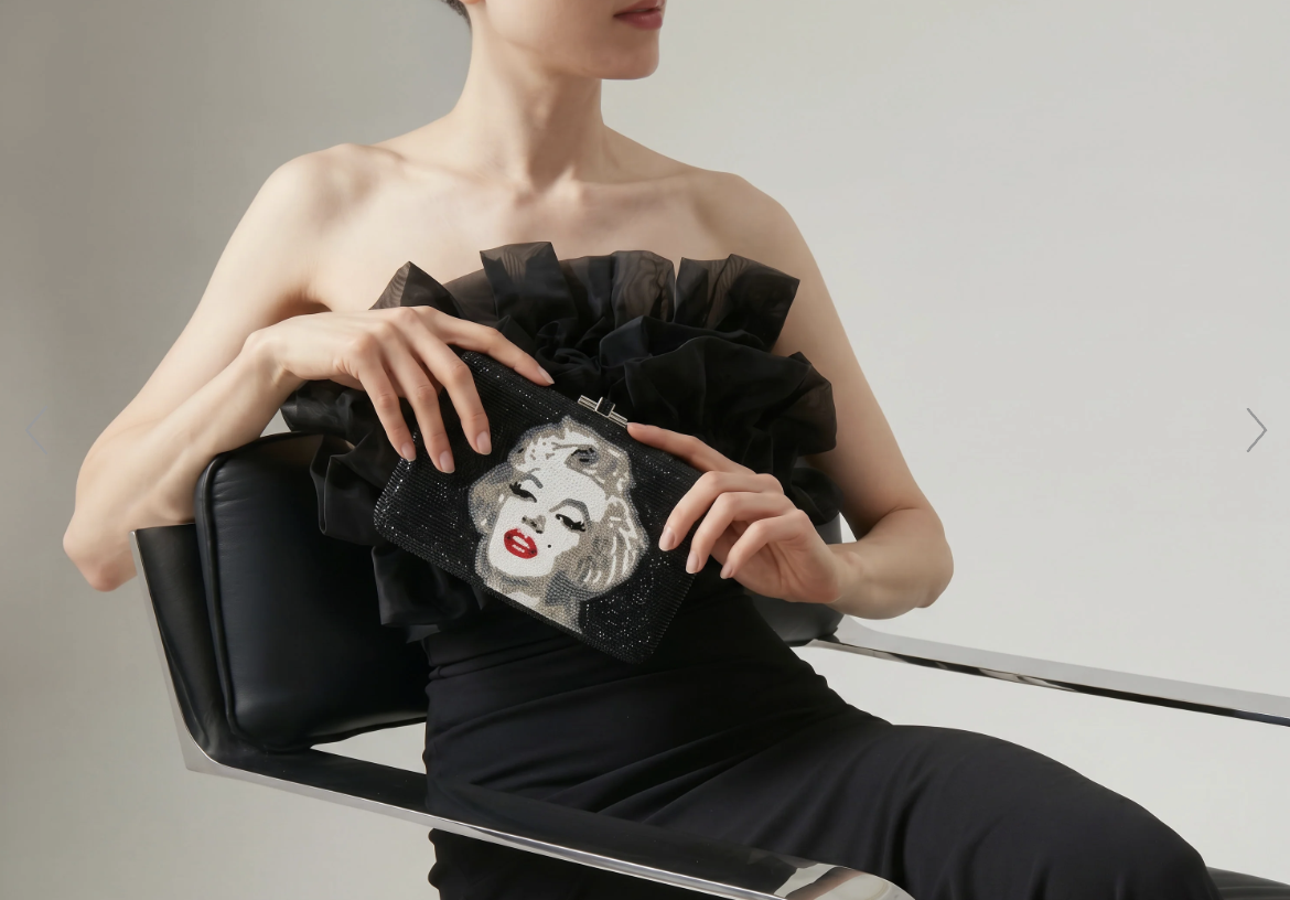 Rebecca Rose wears a black chiffon dress and holds a bejeweled Judith Leiber clutch with an image of Marilyn Monroe on it.