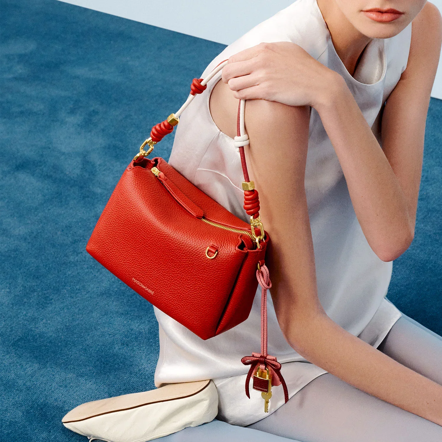 Red shoulder bag on a model, holding a Maison de Sabre shoulder bag