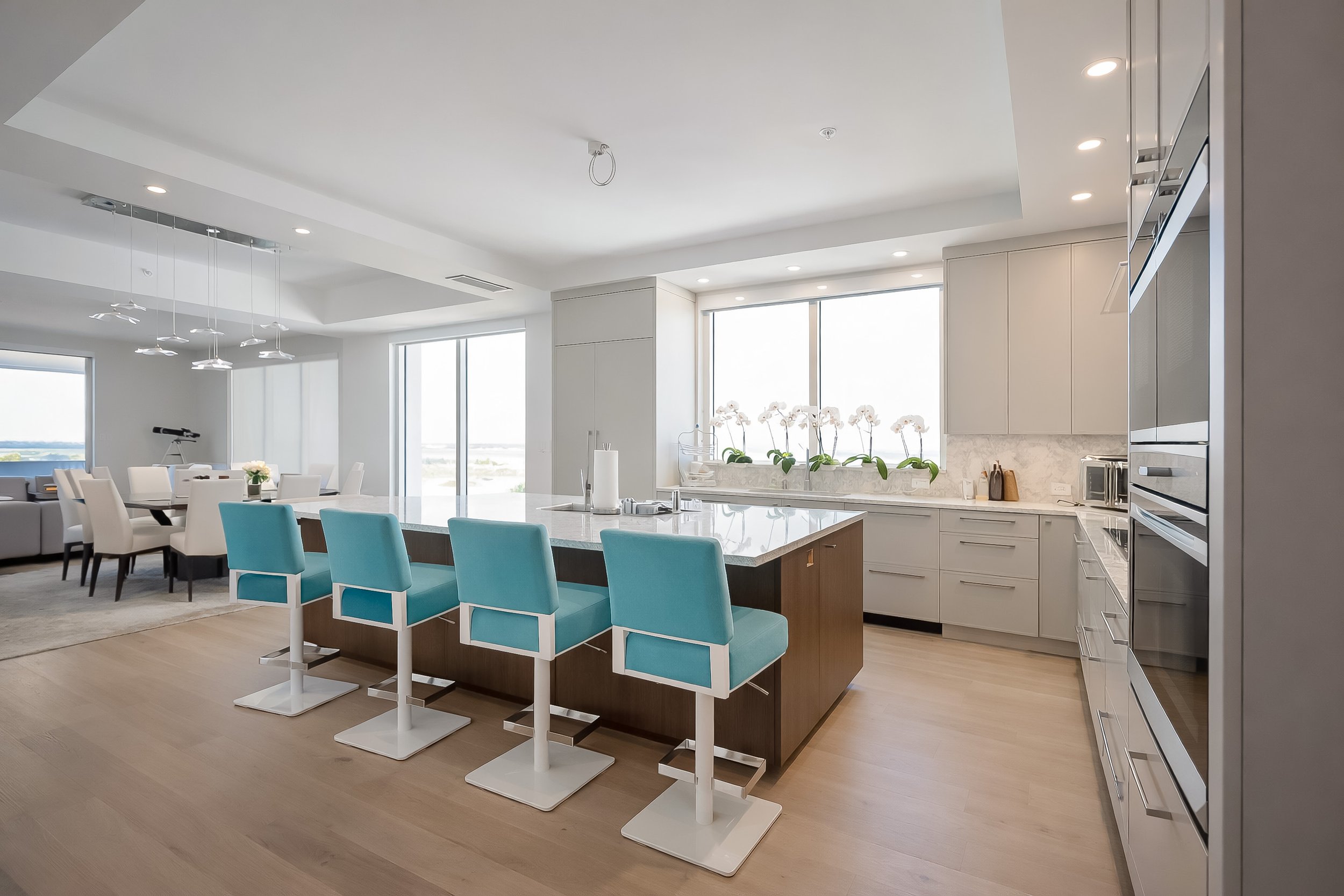 Modern kitchen with white cabinets, marble countertops, kitchen appliances, and a central island, with a dining area visible in the background.