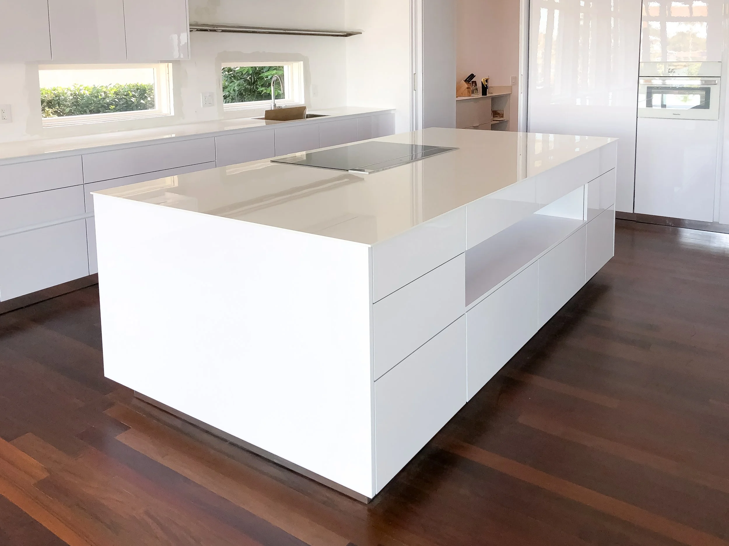 Modern kitchen with white cabinets, marble floor, gray countertop, built-in oven and microwave, black induction cooktop, and a window overlooking greenery.