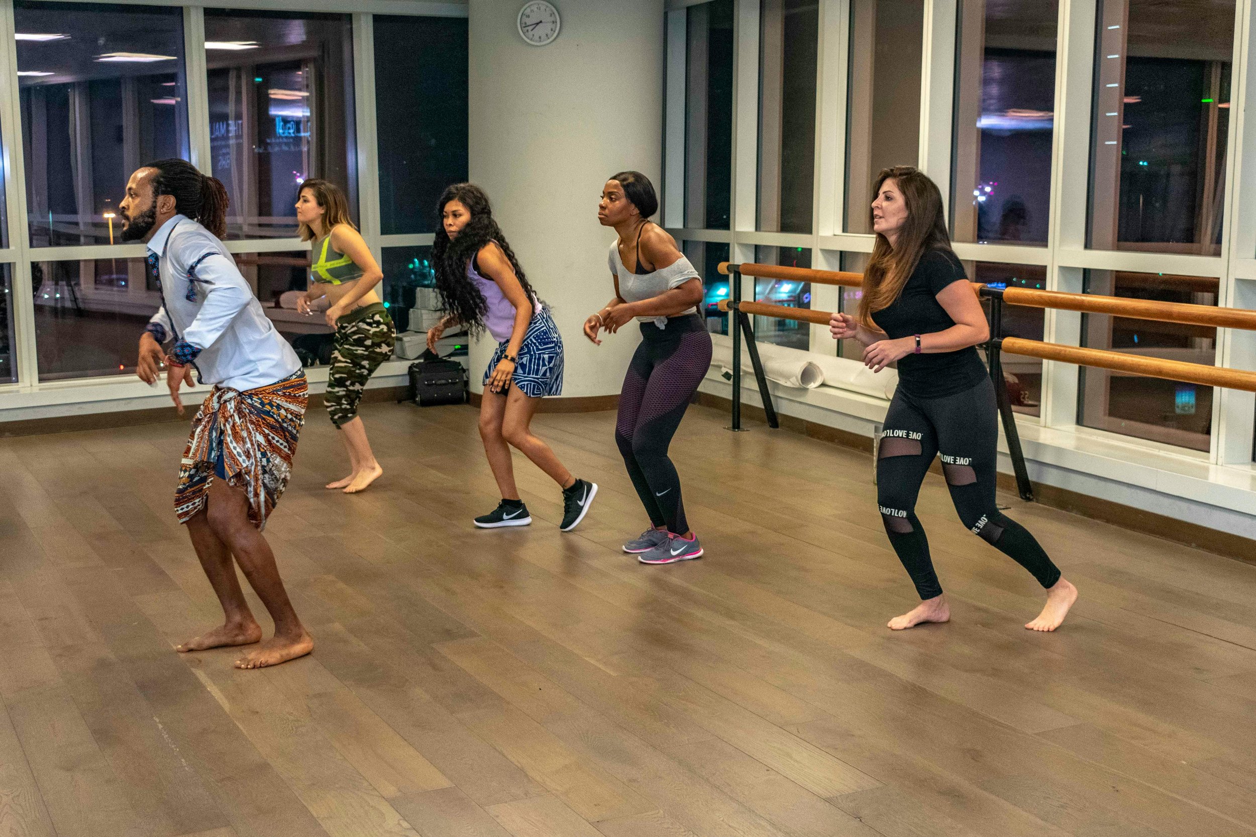 A diverse group of adults dancing or exercising in a dance studio with large windows at night.