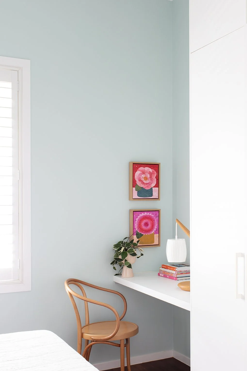 Guest room with pretty mint green walls, colourful artwork, and a classic timber Thonet chair creating a warm and welcoming space