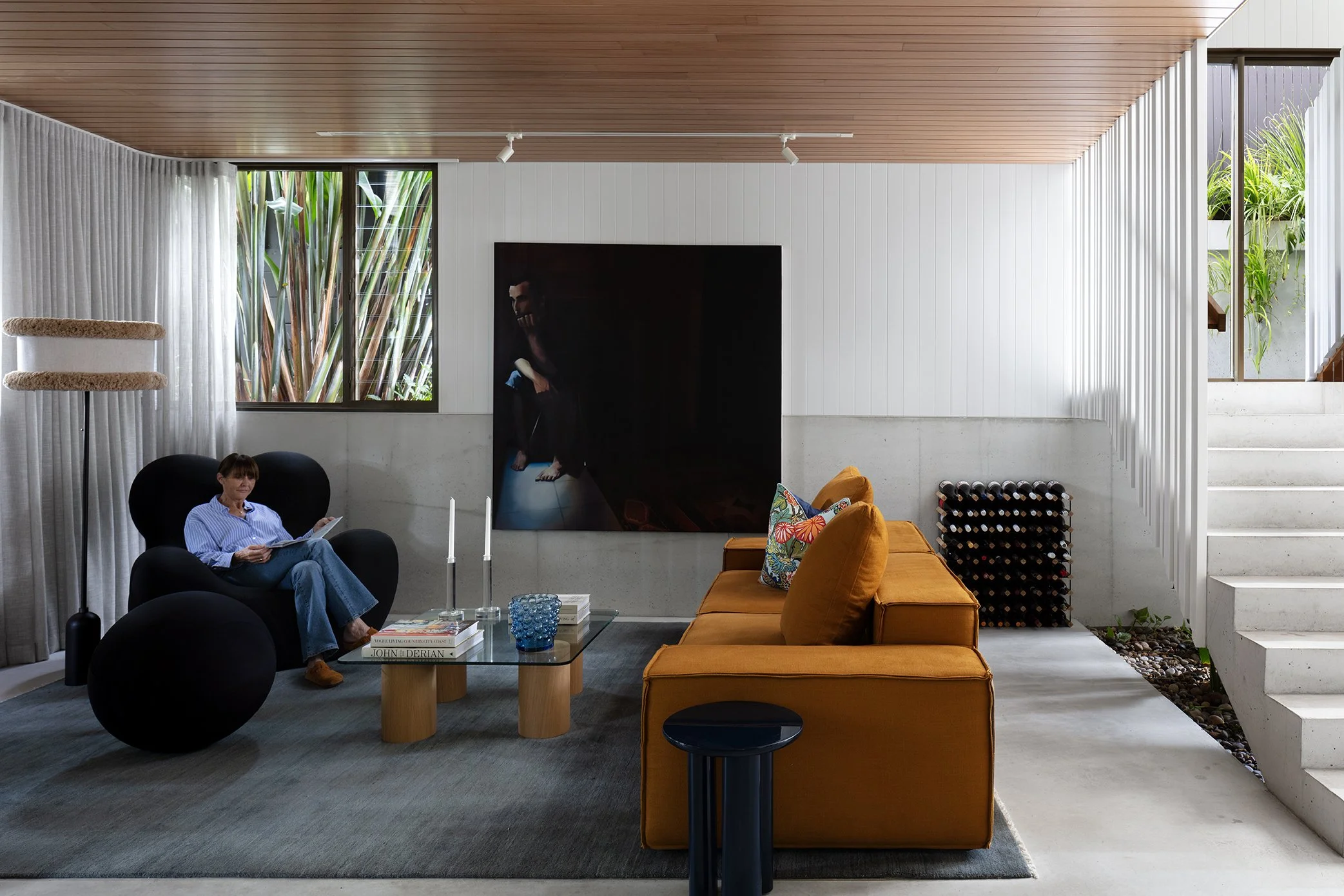 an architect designed home decorated with iconic furniture pieces including a La Mamma armchair in black, a contemporary glass coffee table and rust linen sofa, a lampshade with fringing on a Gubi black metal lampbase, moody artwork