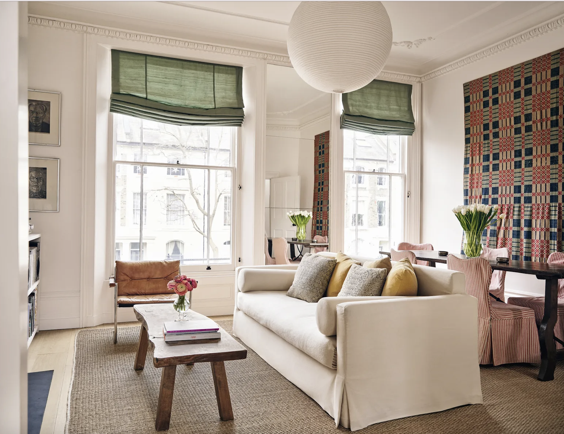 Living room with a cream linen sofa and green relaxed roman blinds, a timber antique coffee table and natural sisal rug, a tapestry on the wall and red and white striped loose cover dining room chairs